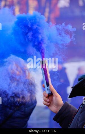 Die Hand hält ein Feuerwerk mit einem Rauch der Farbe blau in einer Masse von Menschen hautnah. Stockfoto