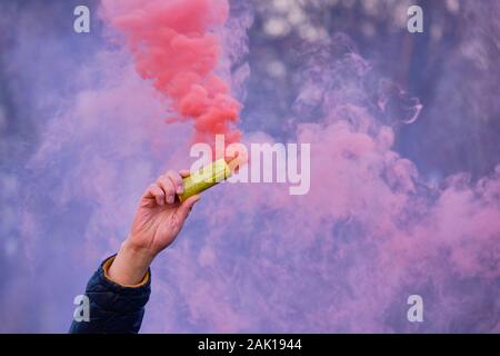 Die Hand hält ein Feuerwerk mit einem Rauch der Farbe rosa. Close Up. Stockfoto