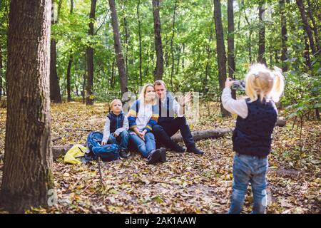 Reisen, Tourismus, Wandern, Technologie und Familie Konzept. Glückliches Kind macht Foto Eltern im Wald. Mama und Papa posieren für Fotos, Tochter Foto nimmt auf Stockfoto
