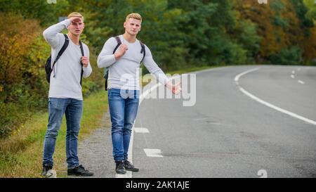 Art des Reisens. Nur Freunde und Straße voran. das Gefühl der Freiheit. Mit Freunden unterwegs. Anreise per Autostop. Hoffnungslos hitchhiker. Männer versuchen stop Auto. Zwillinge zu Fuß entlang der Straße. Wanderer Mann auf der Straße. Stockfoto