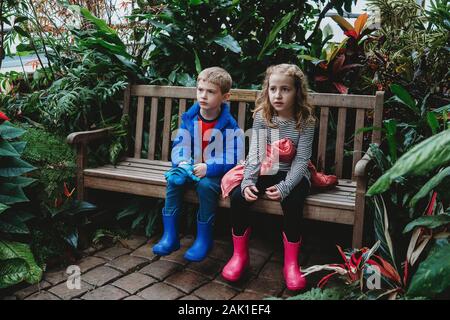 Ein Junge und ein Mädchen sitzen auf einer Bank in einem Gewächshaus. Stockfoto