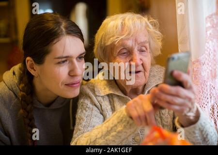 Eine ältere alte Frau sieht ein Smartphone seines erwachsenen Enkelin. Stockfoto