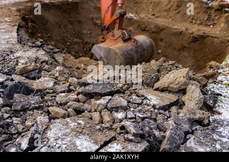 Selektiver Fokus auf der hydraulische Arm eines Mini Bagger bei der Arbeit, graben Graben für Klärgruben und Abflüsse in mit Tieflöffel Hintergrund Stockfoto