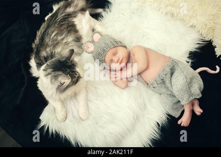 Süßes neugeborenes Mädchen in Maus Kostüm schlafen auf weißem Fell mit cat