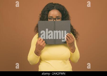 Junge schöne afrikanische Frau tragen Brillen gegen braunen Hintergrund Stockfoto