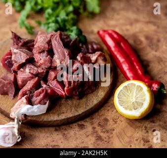 Rindfleisch für Gulasch. Rohes rotes Fleisch auf Holzbrett. Zitrone, roten Pfeffer und Knoblauch. Stockfoto