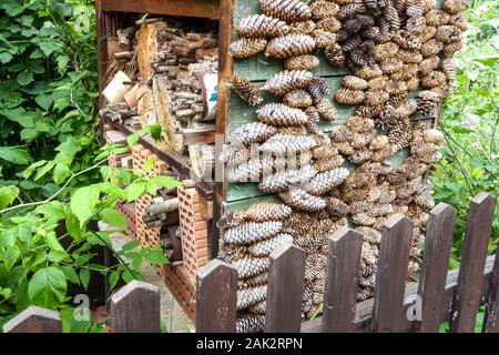 Großes Insektenhotel in einem bewachsenen Garten Holzhaufen Insekten, Zufluchtsort für Nützlinge, Ein Unterschlupf aus verschiedenen Materialien, Kegel, Stiele ... Stockfoto