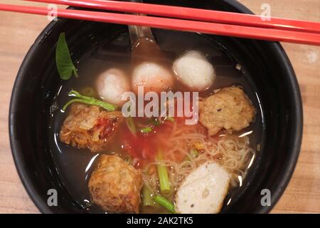 Gelbe Nudeln mit Fisch Fleisch Ball in Rot eine heiße Suppe Stockfoto