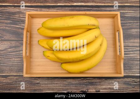 Bündel von reife, gelbe Bananen auf einer hölzernen Fach auf eine Holz- Hintergrund. Nahaufnahme Stockfoto