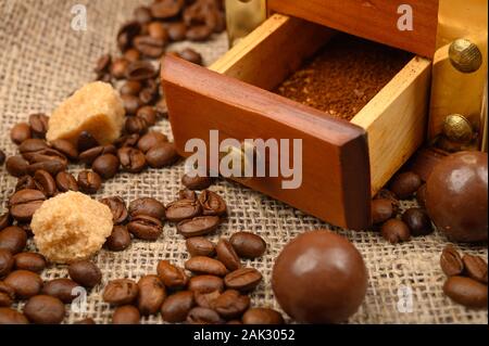 Kaffeemühle, Kaffeebohnen und Schokolade auf dem Hintergrund der rauen handgewebte Gewebe. Nahaufnahme Stockfoto