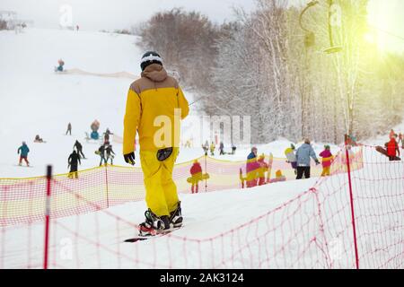 Snowboarder in gelb Skianzug erhebt sich auf heben Sie Berghang. Ski Sport im Winter. Urlaub in den Bergen im Skigebiet. Stockfoto