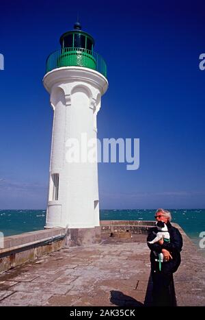 Eine Frau mit einem Hund in ihre Arme steht vor der Light House von St-Valery-en-Caux im Departement Seine-Maritime, Frankreich. (Undatiert pictu Stockfoto