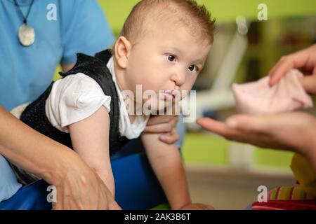 Porträt eines Babys mit zerebraler Lähmung auf Physiotherapie bei Kindern Therapie Zentrum. Jungen mit Behinderung hat die Therapie durch Übungen. Besondere Bedürfnisse. Stockfoto