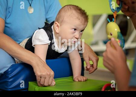 Porträt eines Babys mit zerebraler Lähmung auf Physiotherapie bei Kindern Therapie Zentrum. Jungen mit Behinderung hat die Therapie durch Übungen. Besondere Bedürfnisse. Stockfoto