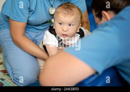 Porträt eines Babys mit zerebraler Lähmung auf Physiotherapie bei Kindern Therapie Zentrum. Jungen mit Behinderung hat die Therapie durch Übungen. Besondere Bedürfnisse. Stockfoto