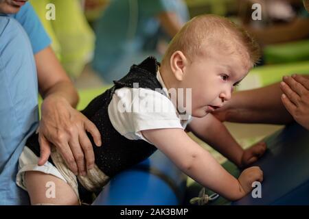 Porträt eines Babys mit zerebraler Lähmung auf Physiotherapie bei Kindern Therapie Zentrum. Jungen mit Behinderung hat die Therapie durch Übungen. Besondere Bedürfnisse. Stockfoto