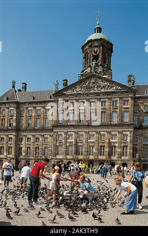 Touristen füttern Tauben vor dem Königlichen Palast (Koninklijk Paleis) am Damm in Amsterdam. Es war im 17. Jahrhundert gebaut. Ursprünglich wurde es hos Stockfoto