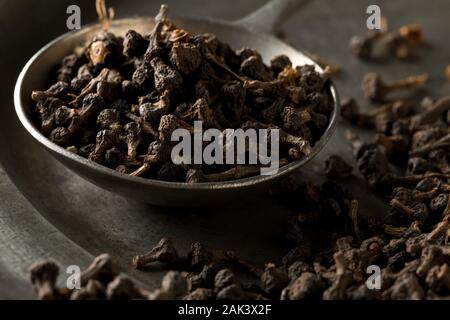 Haufen von roh, getrocknet Zimt blossom buds Gewürz auf Metallplatte mit Metall Schaufel auf rustikalen schwarz Tisch Hintergrund mit selektiven Fokus Stockfoto