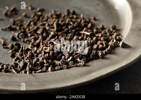 Haufen von roh, getrocknet Zimt blossom buds Gewürz auf Metallplatte auf rustikalen schwarz Tisch Hintergrund mit selektiven Fokus Stockfoto