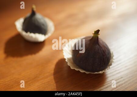 Zwei reife süsse Feigen im Weißbuch auf einem Holztisch. Stockfoto