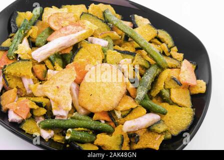 Gebackene Gemüse Chips, süsse Kartoffeln, grüne Bohnen, Taro und Squash in einen schwarzen Schüssel gehören. Auf weiß isoliert. Stockfoto