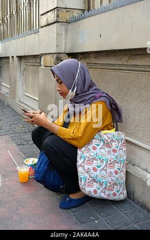 Jakarta, Indonesien - 2019.12.20: eine junge Frau mit Kopftuch ruhenden Hocken auf dem Bürgersteig an der Jalan teluk betung 1 Während in der Innenstadt Stockfoto