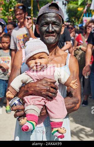 Ibajay Town, Provinz Aklan, Philippinen: Alter Mann mit schwarzem Gesicht, der eine Babypuppe auf der Ati-Atihan Festival Street Parade hält Stockfoto