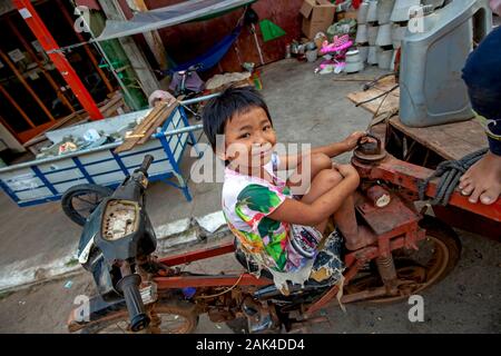 Einem armen Mädchen, deren Obdachlose Familie scavenges für wieder verwertbare Material sitzt auf einem Motorrad Sitz vor ihr Tierheim in Kampong Cham, Kambodscha. Stockfoto