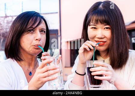 Junge weibliche Freunde multi-ethnischen nehmen einen Aperitif im Freien beim Sprechen und Lachen Stockfoto