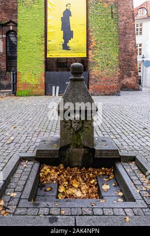 Kopenhagen, Dänemark. Granit Brunnen außerhalb der Nikolaj Kirche auf der Højbro Plads square 1899 installiert. Leonard Cohen Plakat zur Ausstellung Stockfoto