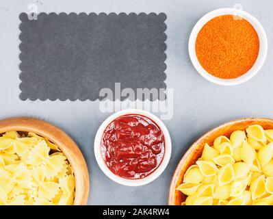 Verschiedene Arten von Nudeln in Holzschalen, roter Chili, Tomatensauce auf grauem Beton Hintergrund mit kopieren. Gesunde Ernährung Konzept Stockfoto