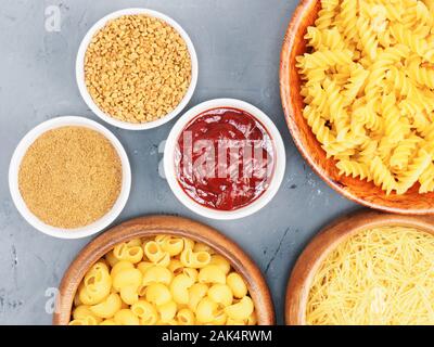 Verschiedene Arten von Nudeln in Holzschalen, Tomatensauce, Bockshornklee, Masala auf grauem Beton Hintergrund mit kopieren. Gesunde Ernährung Konzept Stockfoto