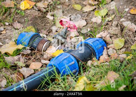 Bewässerungsanlagen, Herbst Boden mit braunen Laub, blau Verbindungen von Schwarzen, die in kaltem Wasser Rohr- und rostigen Hahn mit rotem Griff, close-up gegen Erde Hintergrund. Zlato Pole, Bulgarien, Europa Stockfoto