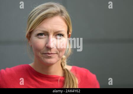 Schwerwiegende attraktive Langhaarige, blonde Frau aufmerksam in die Kamera starrte mit geöffneten Lippen gegen eine graue Wand mit Kopie Raum Stockfoto