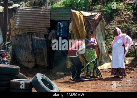 Menschen vor einer sehr einfachen Motorradwerkstatt in einer Wellblechscheune in Conakry, Guinea, Westafrika Stockfoto