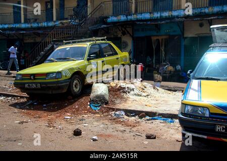 Blick auf gelbe Autos, die auf Müll und Müll neben der Straße vor einem Apartmentgebäude in Conakry, Guinea, geparkt sind Stockfoto