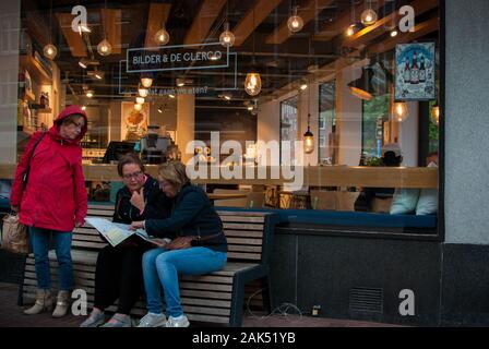 Drei Frauen auf der Bank vor einem Restaurant suchen nach Wegbeschreibungen auf einer Karte sitzt Stockfoto