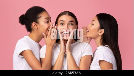 Drei tausendjährigen Mädchen teilen Geheimnisse Flüstern Gerüchte und Klatsch über Pink Studio Hintergrund stehen. Panorama Stockfoto