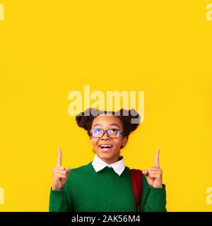 Für Ad. Aufgeregt afro jugendlich Mädchen zeigen auf Copyspace über Gelb Hintergrund isoliert, Bild vertikal Stockfoto