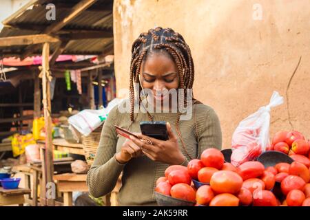 Junge afrikanische Frau verkaufen in einer lokalen afrikanischen Markt mit ihrem Mobiltelefon und Kreditkarte Stockfoto