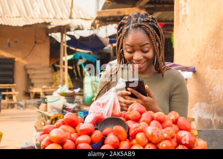 Junge afrikanische Frau in einer lokalen afrikanischen Markt Anzeigen von Inhalten auf Ihrem Handy und überrascht Stockfoto