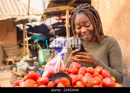 Schöne junge afrikanische Frau in einer lokalen afrikanischen Markt Anzeigen von Inhalten auf Ihrem Handy überrascht Stockfoto