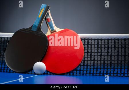 Zwei Tischtennisschläger und Bälle auf einem blauen Tisch mit Netz. Stockfoto