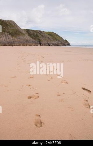 Eine breite Sandstrand mit Footprints in Richtung zu den Fernen Klippen an Drei Zinnen Bucht auf der Halbinsel Gower, Wales Stockfoto