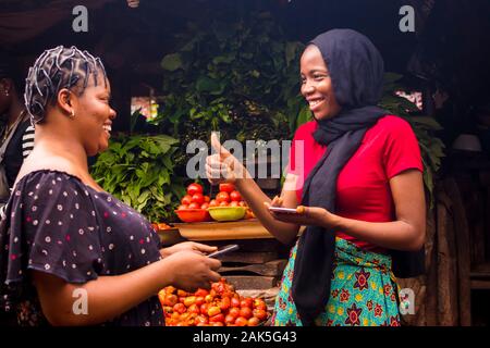 Afrikanische Frau verkaufen in einem lokalen Markt gibt einen Daumen bis zu einem Kunden erfolgreicher Zahlung per Handy Übertragung zu bestätigen Stockfoto