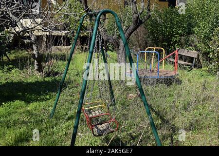 Alte schaukeln rusty Merry-go-round und Holzbank in verlassenen überwachsen Kinderspielplatz. Stockfoto