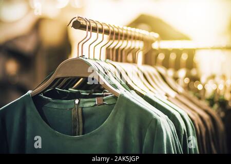 Auf Kleiderbügeln im Bekleidungsgeschäft hängen Modische grüne Kleider, durch künstliches Licht beleuchtet. Stockfoto