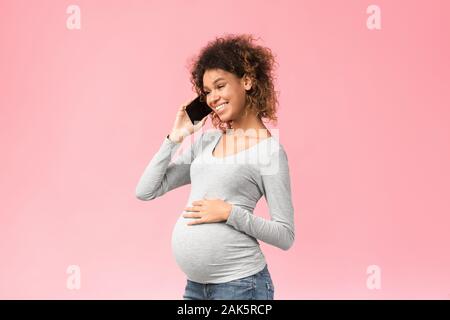 African-american schwangere Frau mit Telefongespräch und berühren Bauch über Pink Studio Hintergrund Stockfoto