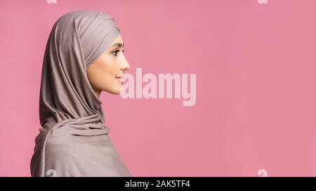 Muslimische Schönheit. Profil Portrait von bescheidenen islamische Mädchen im hijab bei copy space Blick auf rosa Hintergrund, Panorama Stockfoto