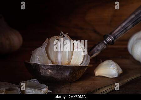 Knoblauch in einem alten silbernen Löffel, Schöpfkelle auf alten Hackklotz.. Dunkle Moody Stockfoto